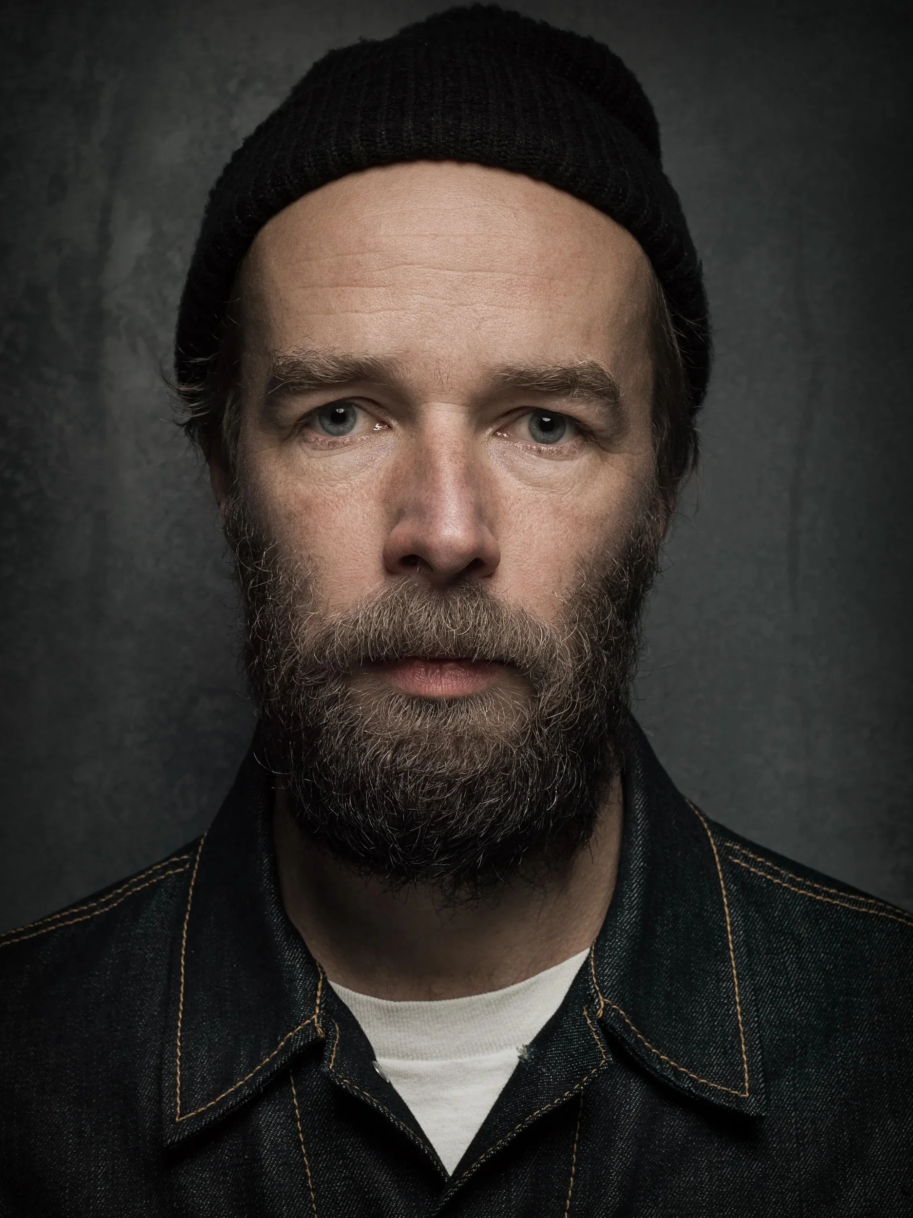 Close-up portrait of a man wearing a black beanie in soft studio light.